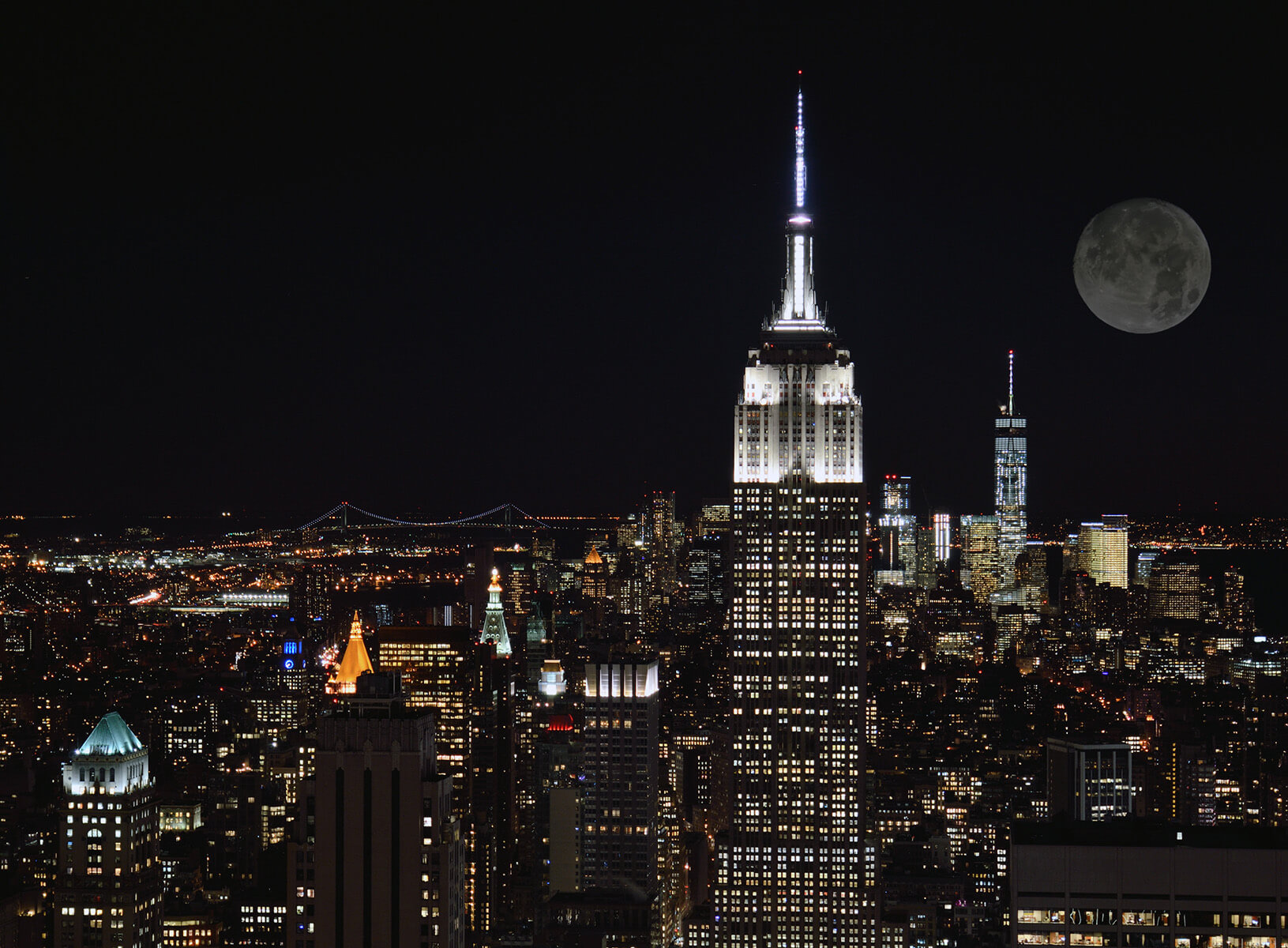 Nighttime city skyline featuring the Empire State Building illuminated alongside other skyscrapers and a full moon in the sky.